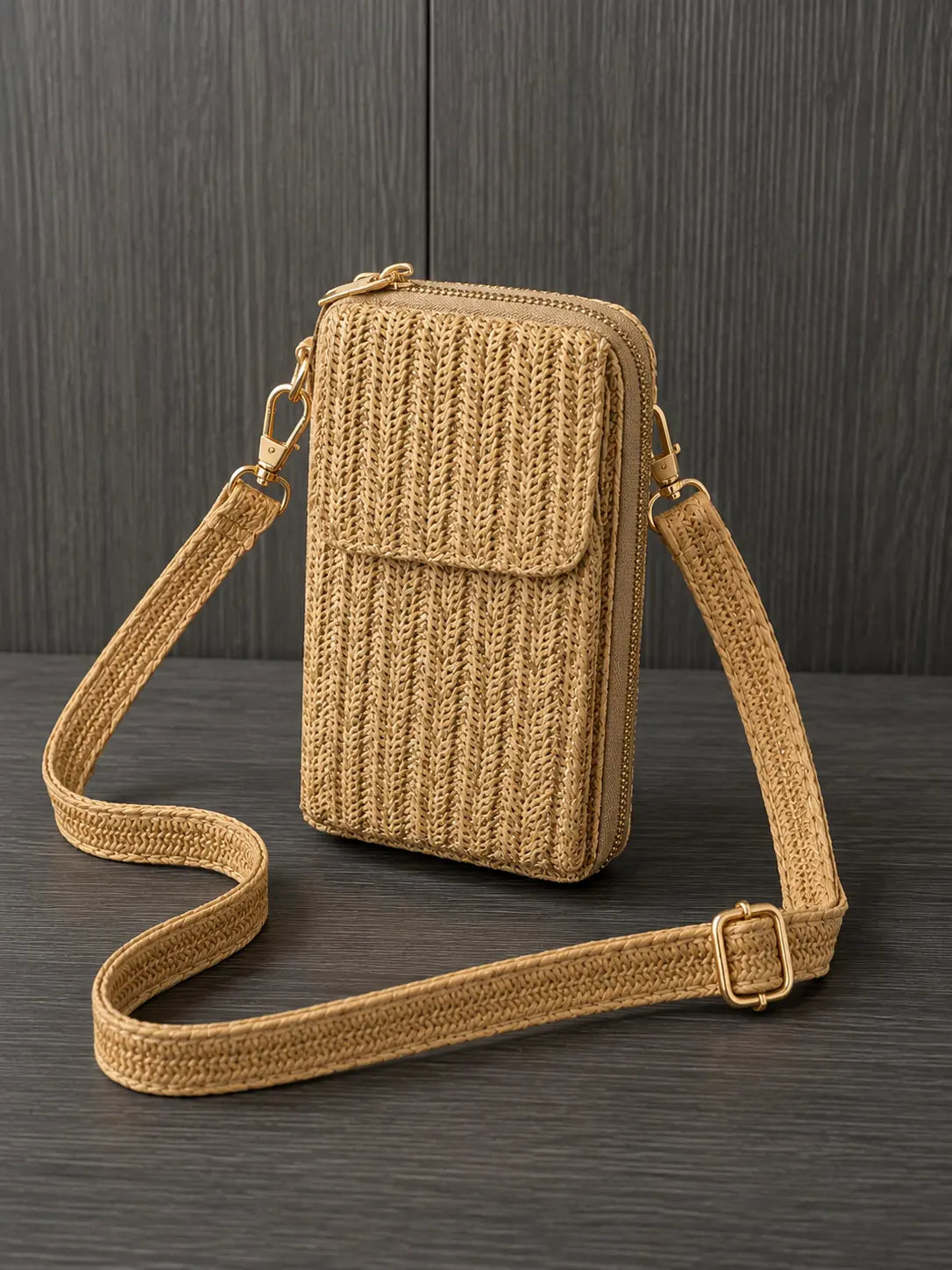 Sac portefeuille bandoulière beige tressé avec poche téléphone et fermeture zippée posé sur fond bois foncé.